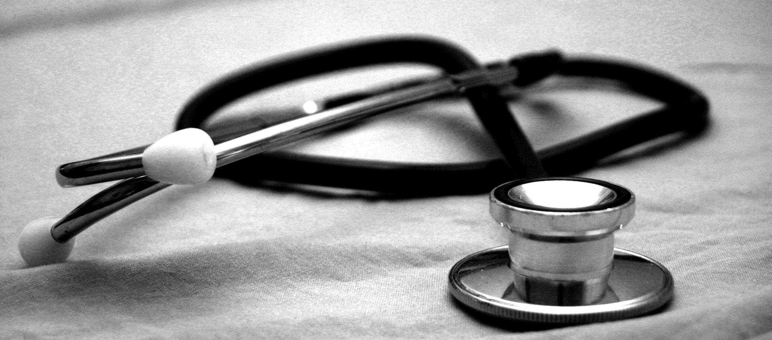 Stethoskop liegt auf einem Krankenhausbett-Laken, Nahaufnahme, Schwarz-Weiß-Fotografie